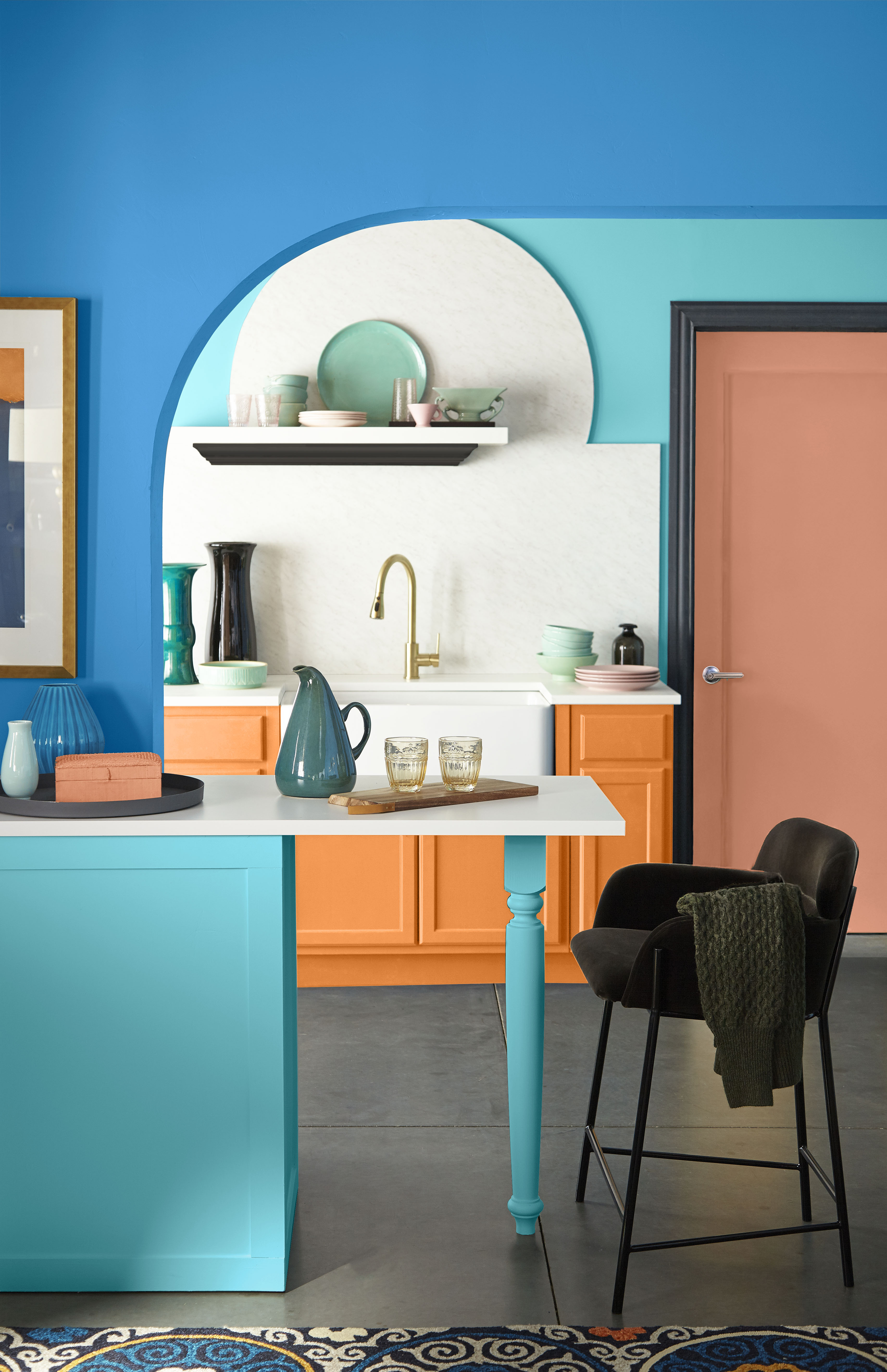 Colourful kitchen nook with orange cabinets, blue walls, and a terracotta-coloured door.
