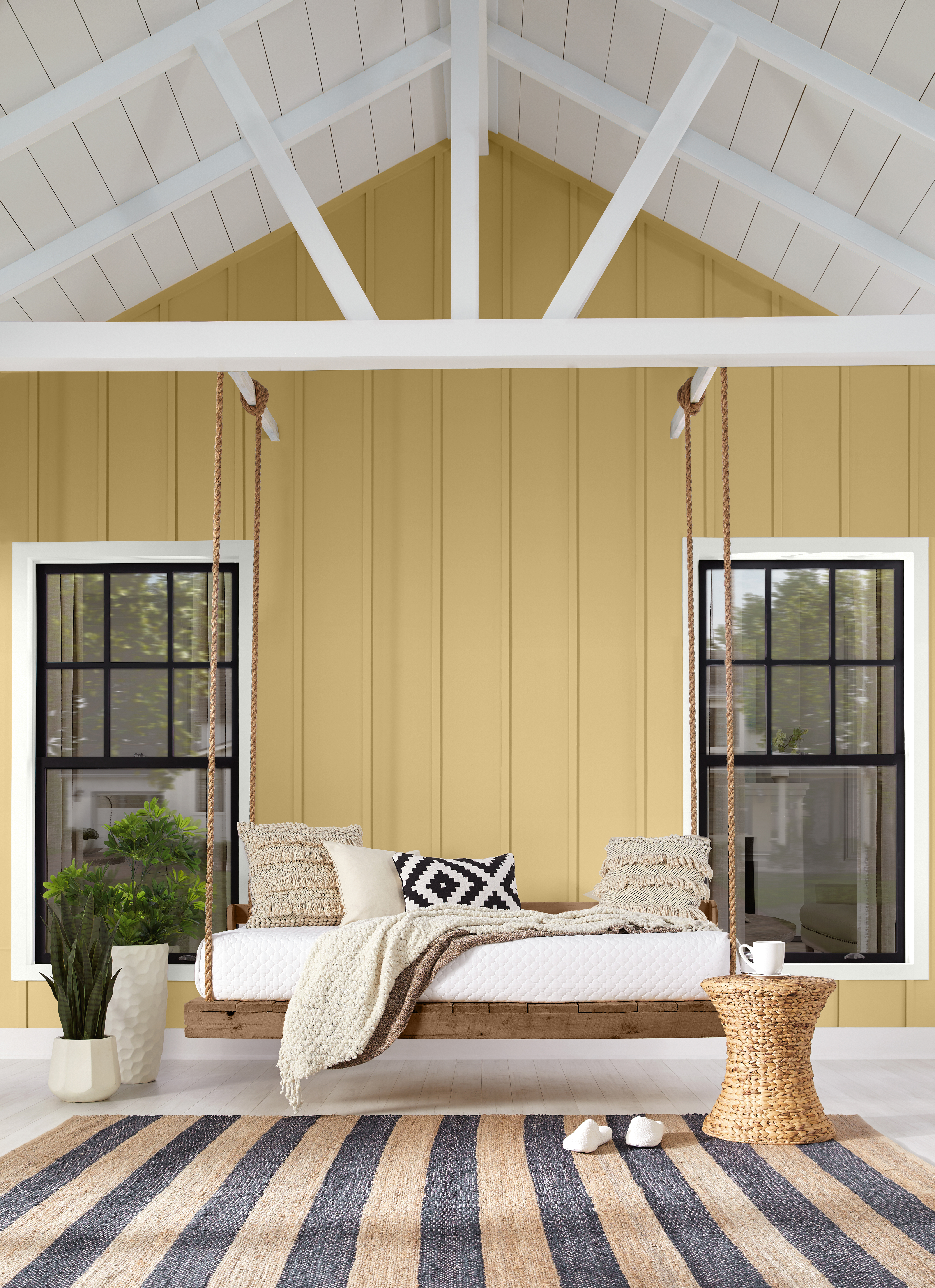 Alt text: A natural wood swing hangs against a warm golden home with light trim.