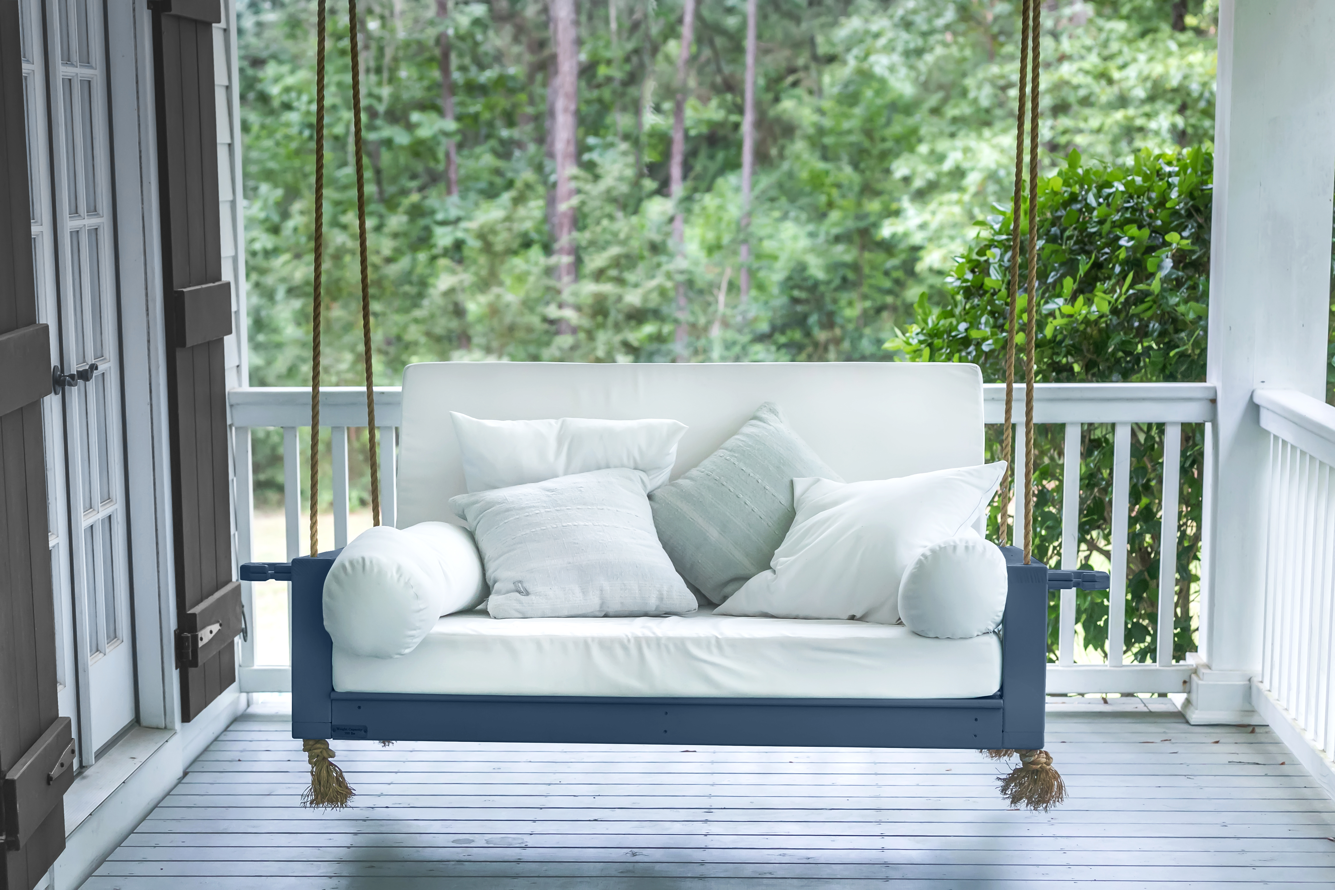 Alt text: A dark navy swing chair contrasts with a soft white cushion and decorative pillows.
