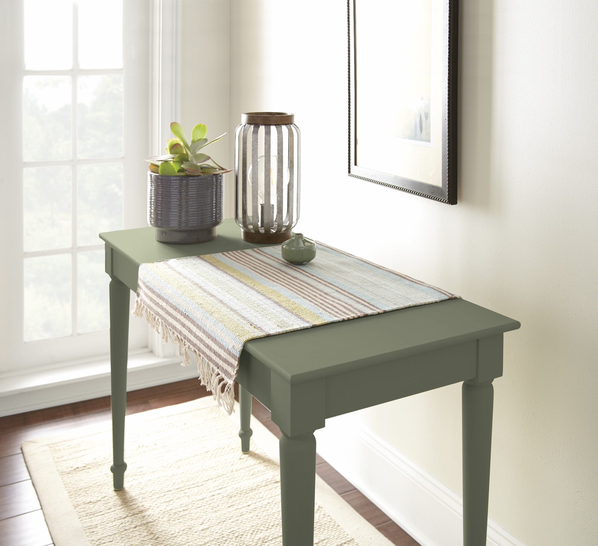 A console table painted in “Ecological,” styled with a plant, decorative accents, and a woven runner in a light-filled hallway.