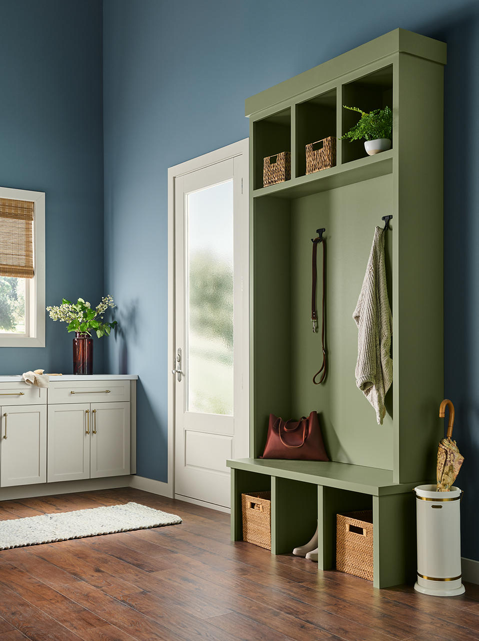 A mudroom back entry with built-in storage painted in “Ecological,” featuring cubbies, hooks, and bench seating against soft blue walls.