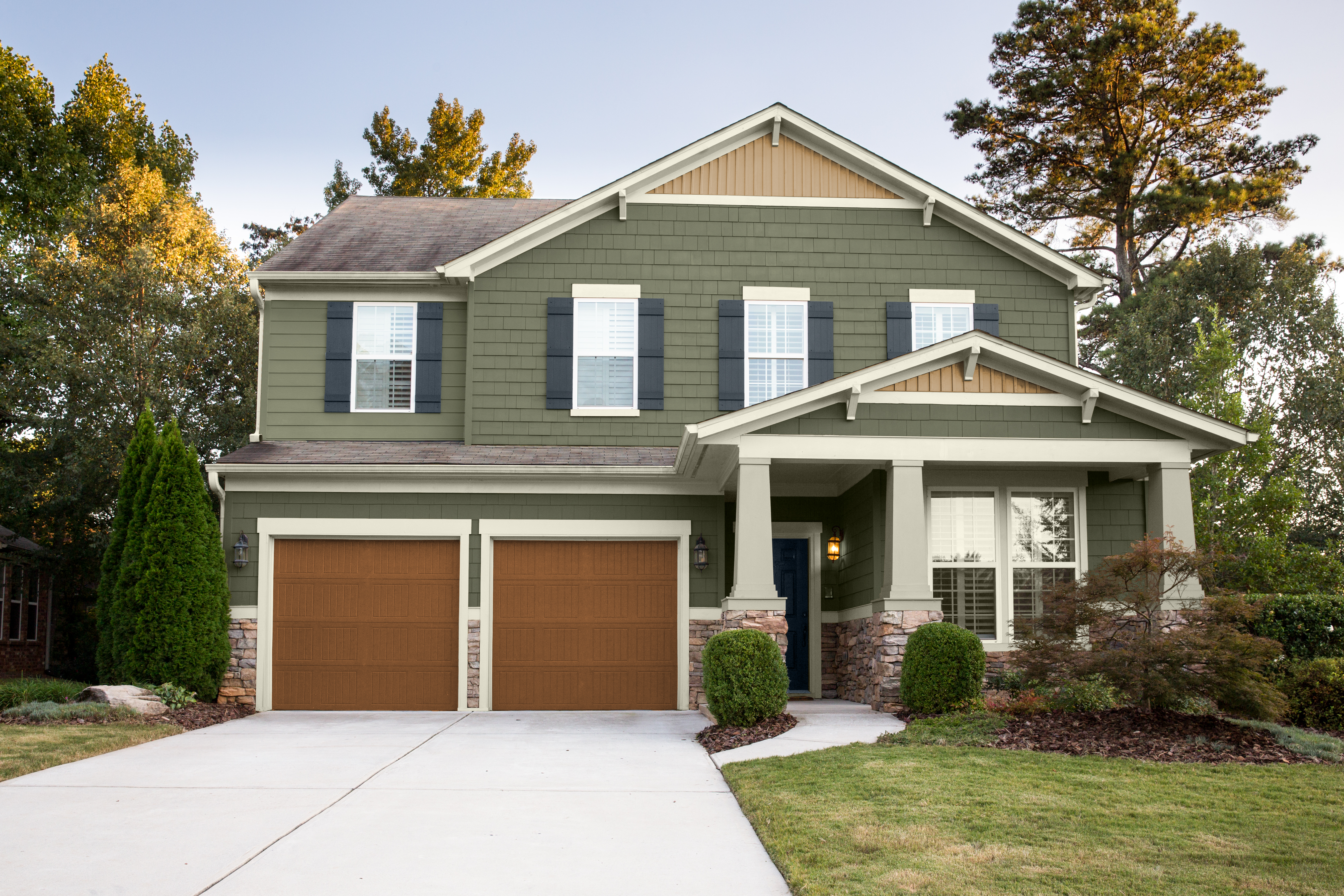 A two-story mostly green colour Craftsman-style home with a double garage, covered front porch, and landscaped yard.