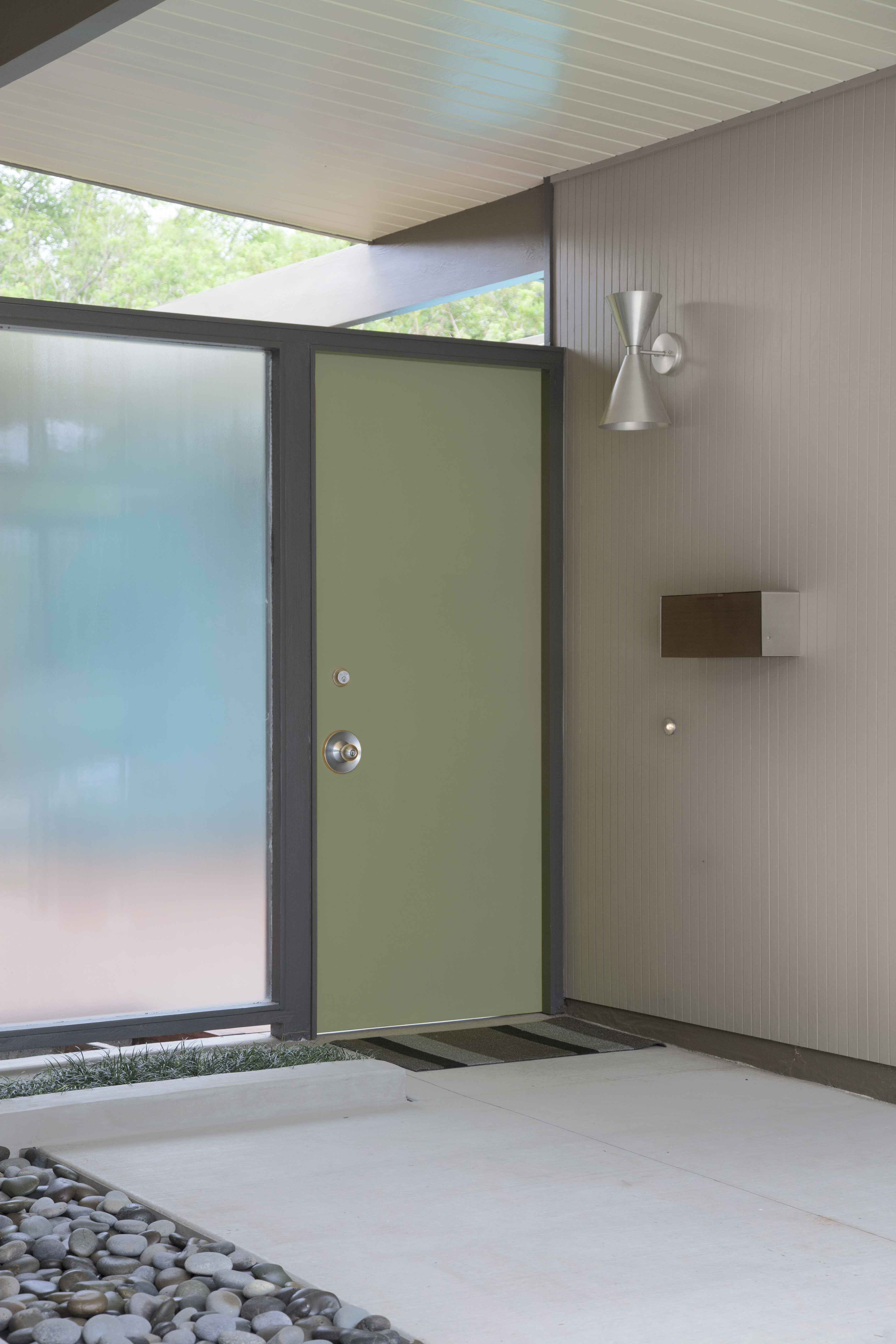 A Mid-century modern entryway with a green front door, frosted glass panels, brown siding, and concrete walkway.