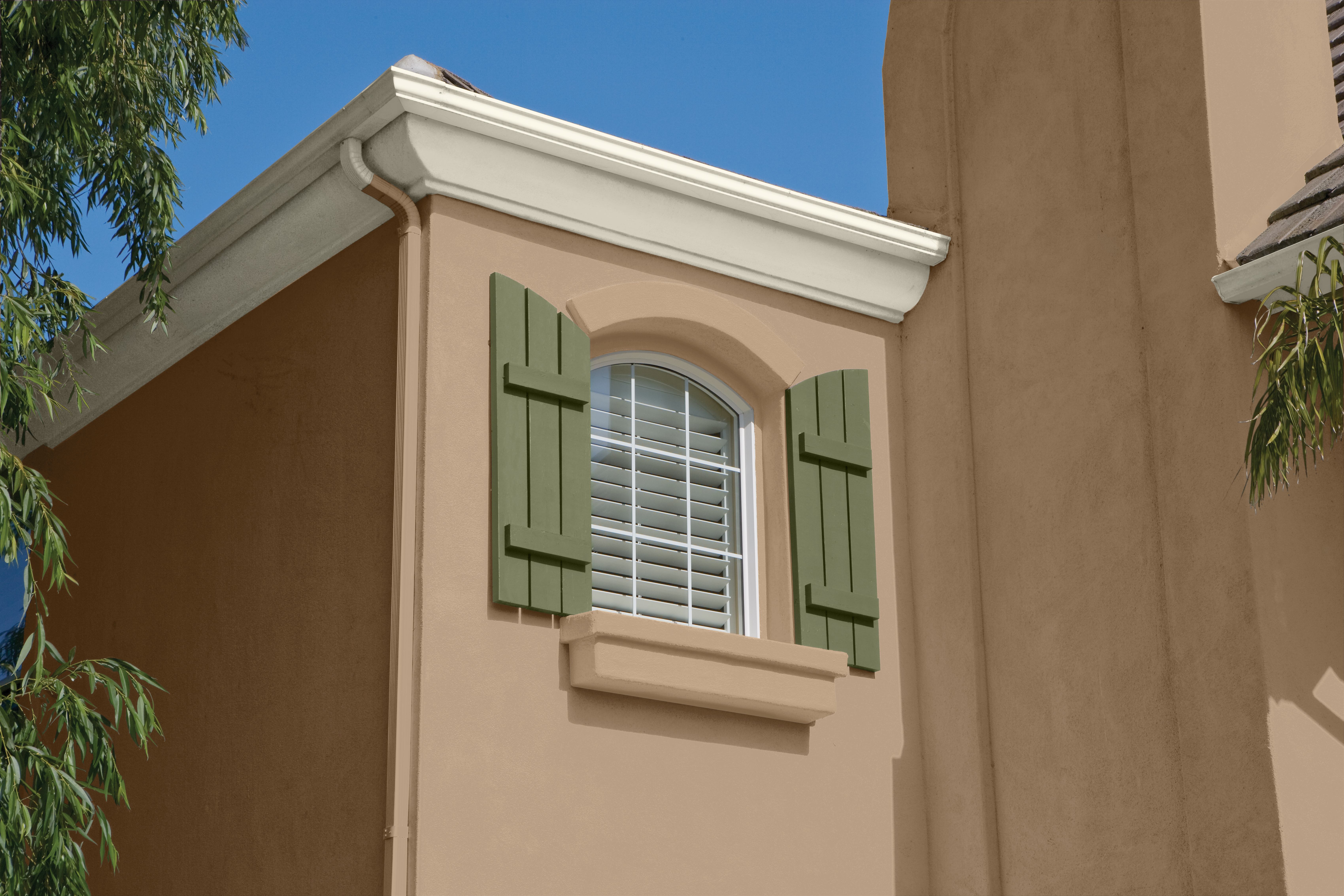 A beige stucco exterior with an arched window, white blinds, and green decorative shutters.