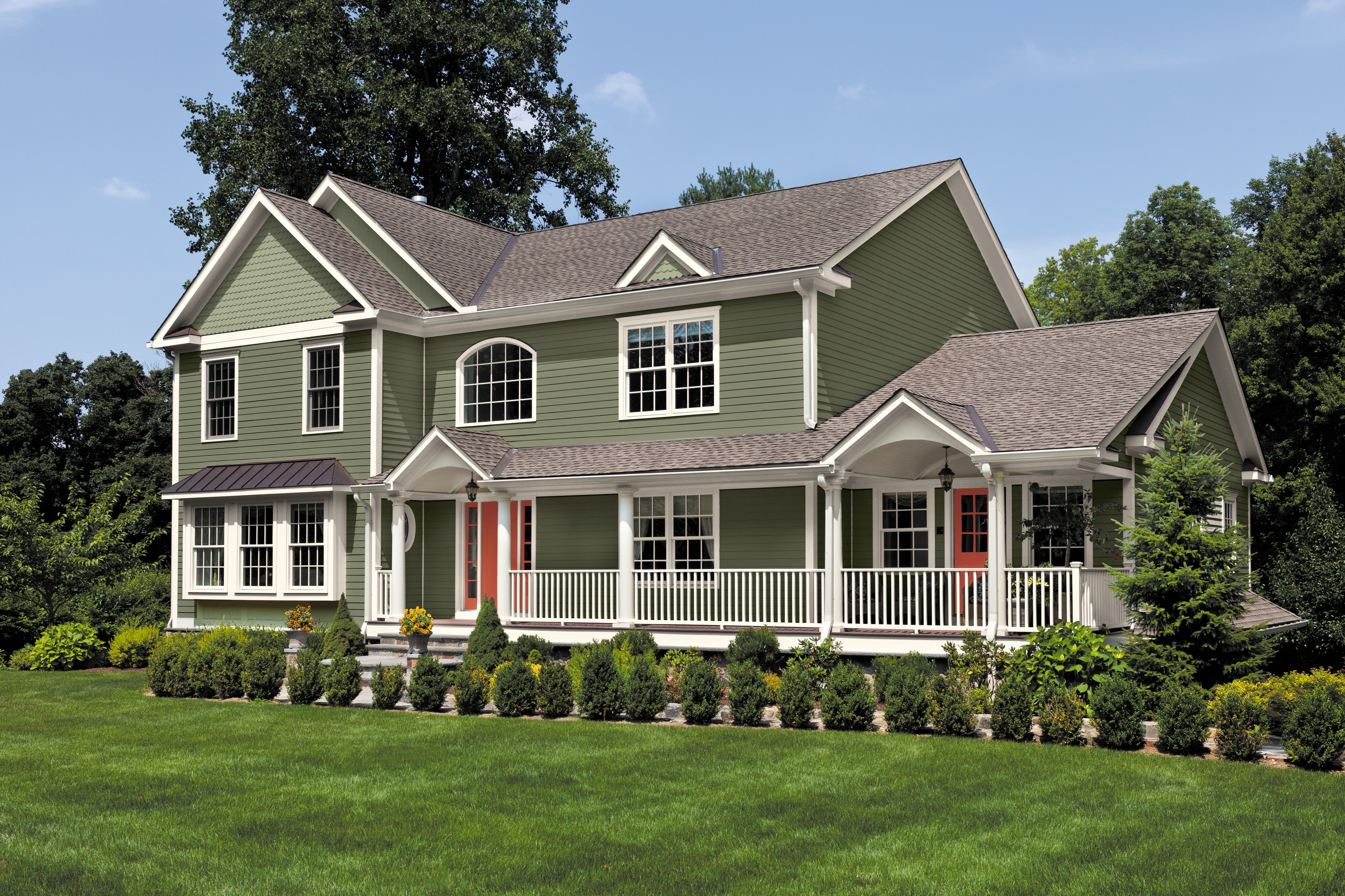 A large light green two-story home with white trim, wraparound porch, red front doors, and manicured lawn.
