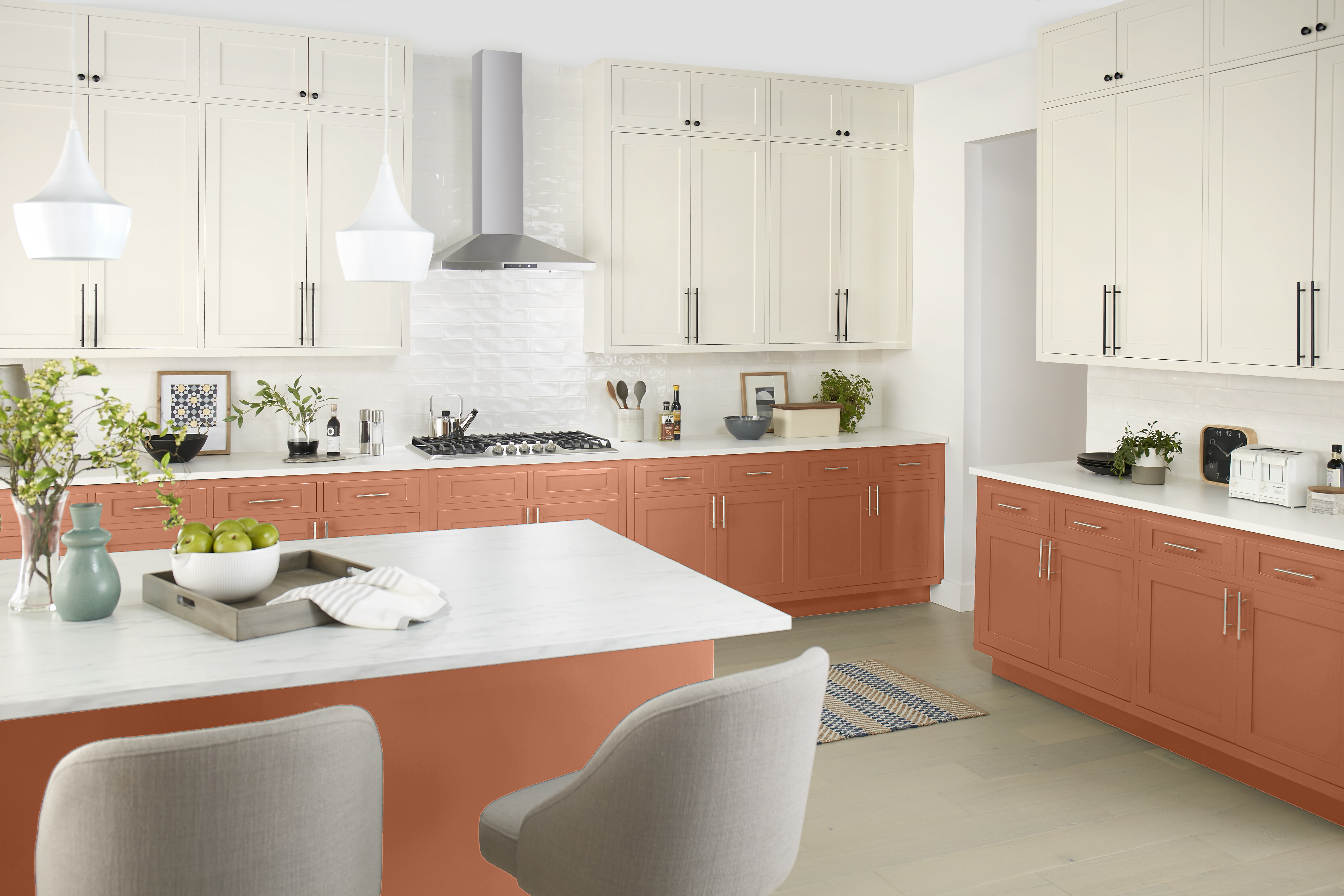 A bright kitchen with warm terracotta paint colour on the lower cabinets, creamy upper cabinets, white countertops, and modern pendant lighting.