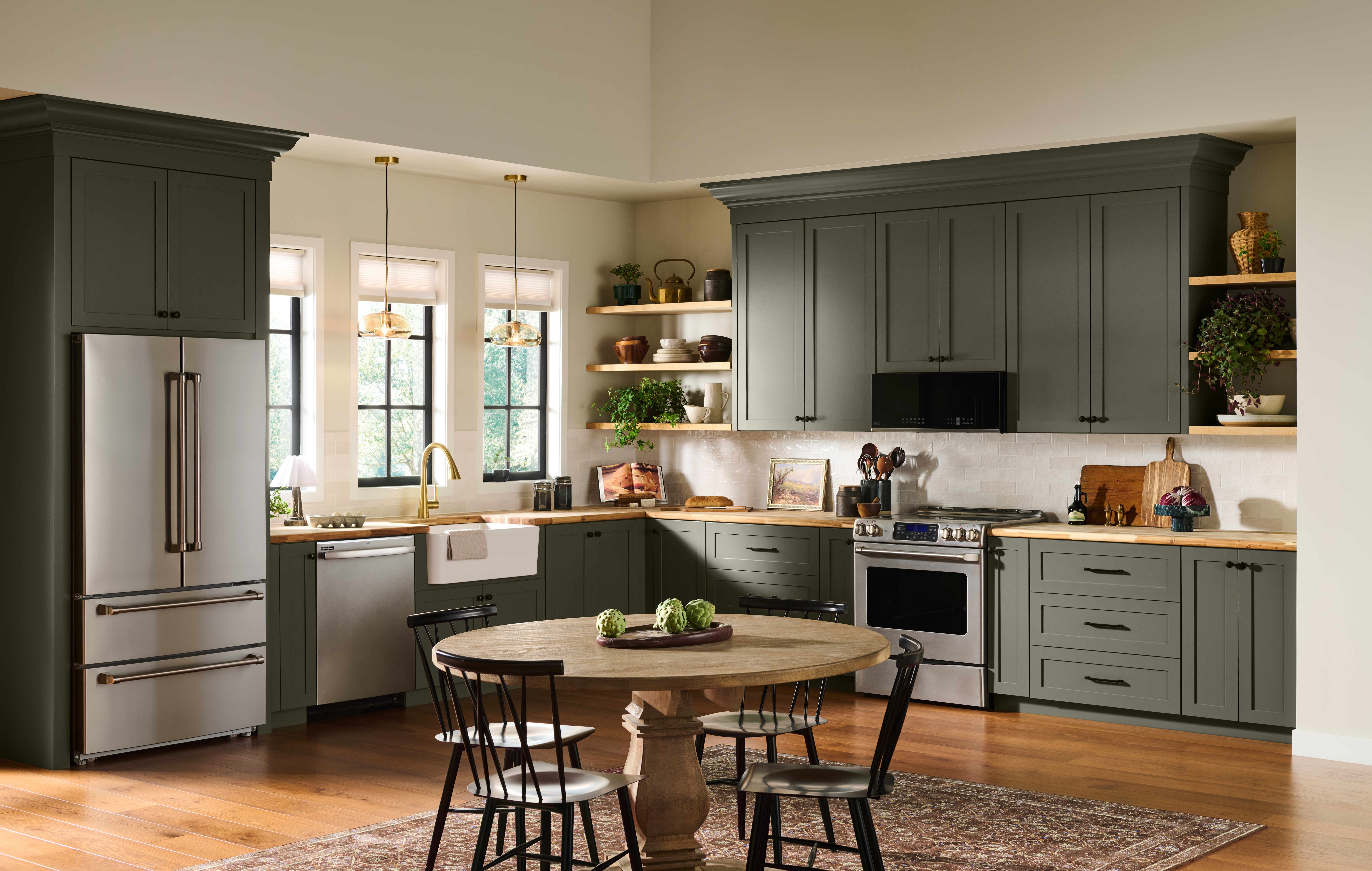 A welcoming kitchen with cabinets painted in BEHR Grounded, featuring warm wood countertops, open shelving, stainless steel appliances, and a round dining table.