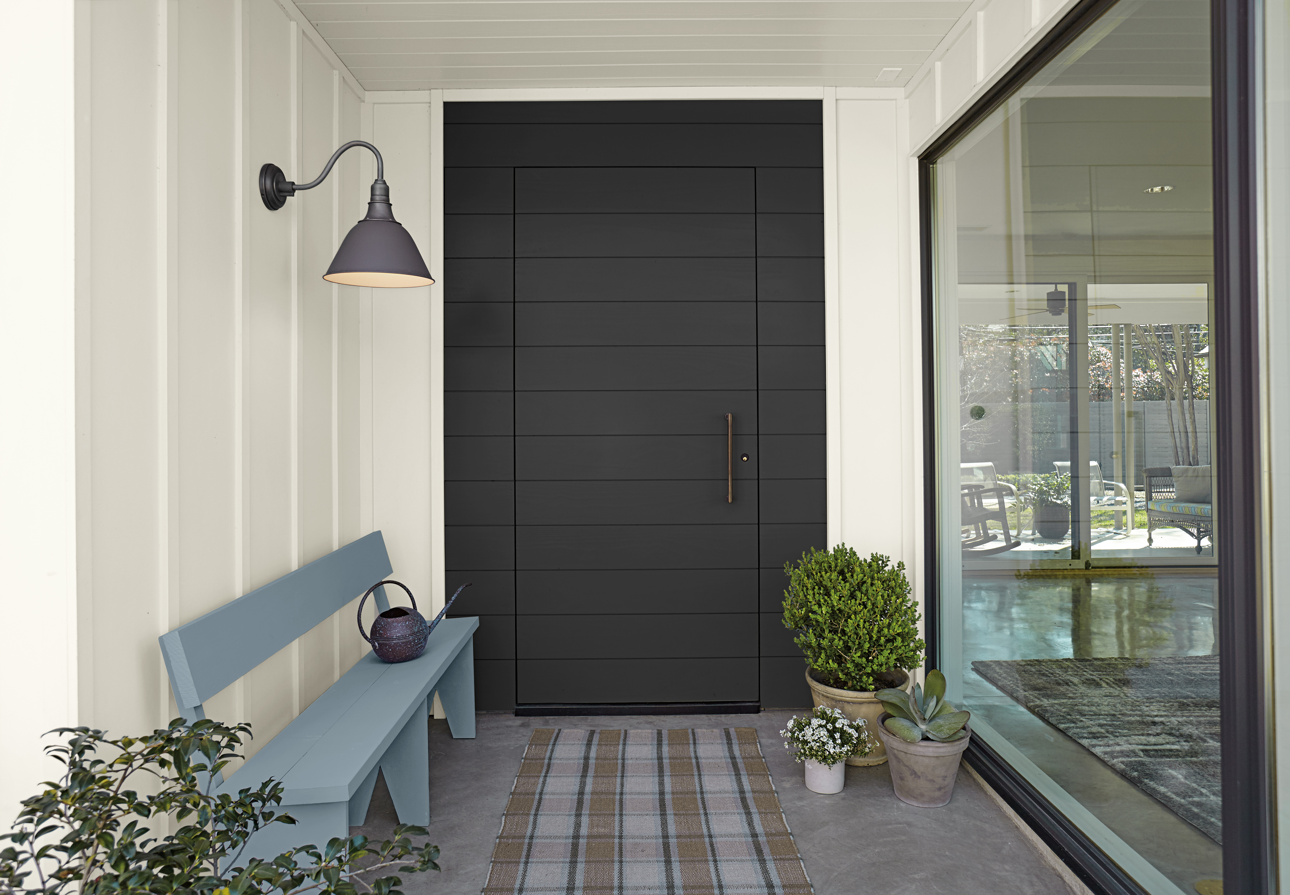 An inviting entryway with a bold, dark front door, soft neutral siding, and a pop of colour from a painted bench.