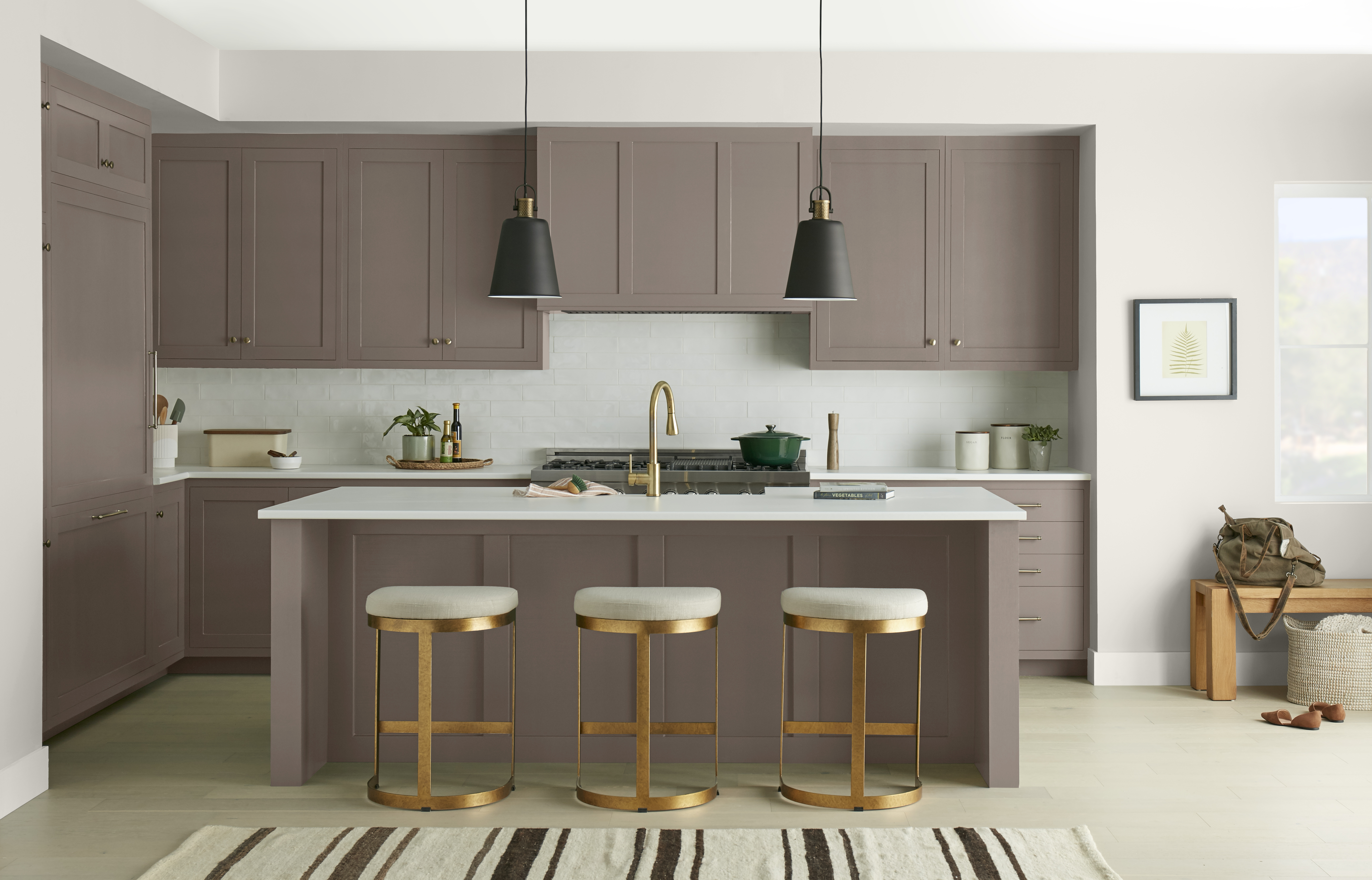An elegant taupe-brown kitchen featuring floor-to-ceiling cabinetry, a matching island, white countertops, brass accents, and black pendant lights. The layered neutral tones create a refined and sophisticated atmosphere.