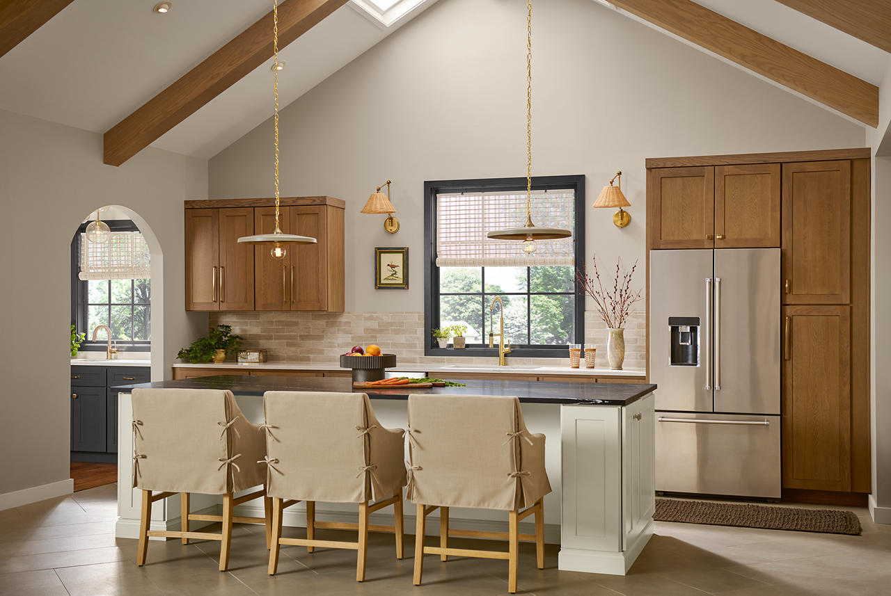 A neutral greige kitchen with layered warm wood cabinets, creamy island cabinetry, beige backsplash tile, brass lighting, and dark charcoal grey accents. The mix of warm greige walls, natural wood tones, and almost-black trim adds depth, making the neutral palette feel balanced, textured, and dimensional.