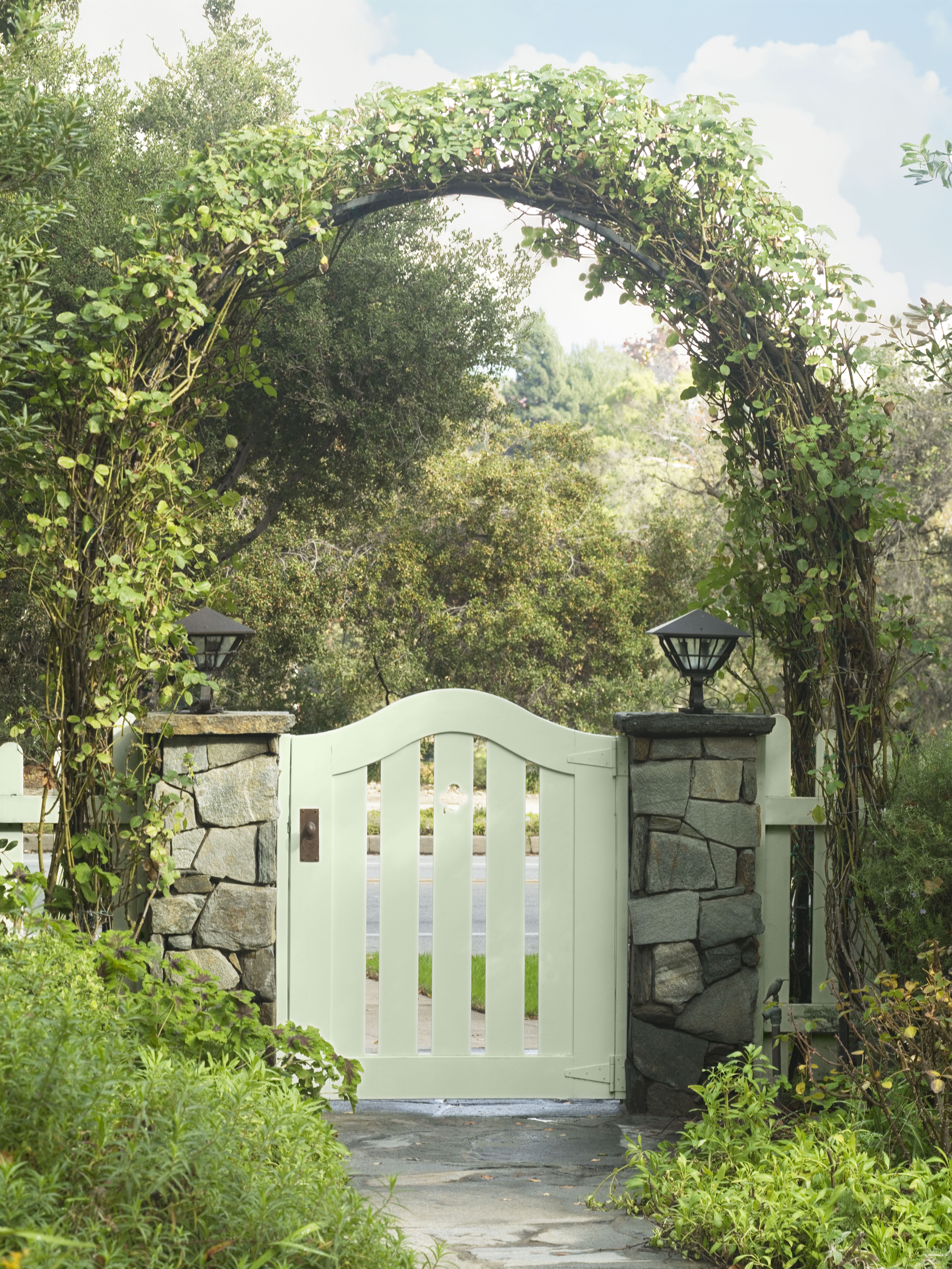 Exterior garden gate painted in a pale cabbage-inspired green, surrounded by stone, greenery, and natural landscaping for an indoor-outdoor colour palette connection.
