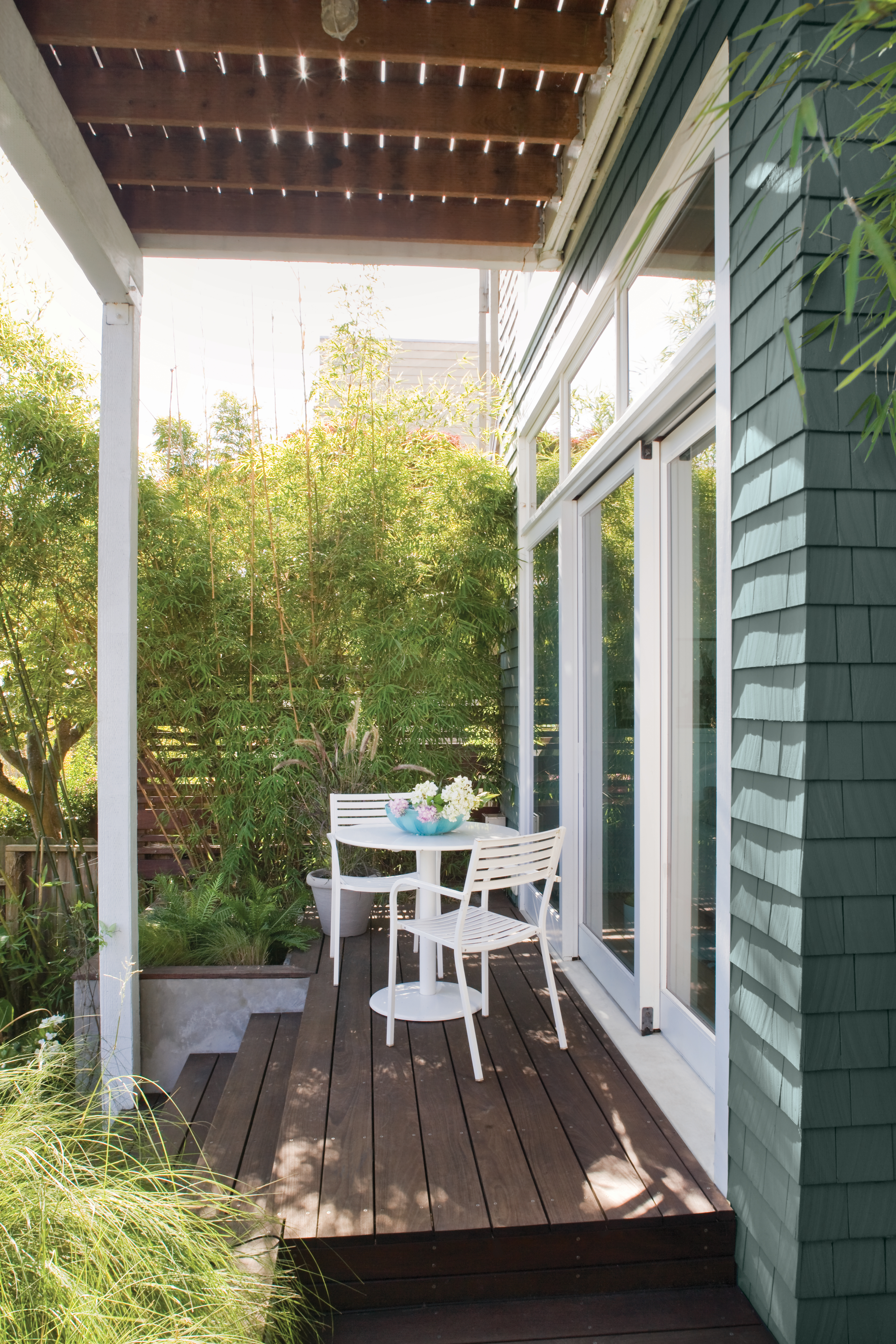 A serene outdoor area featuring a muted green-grey exterior paired with warm wood tones and crisp white trim.