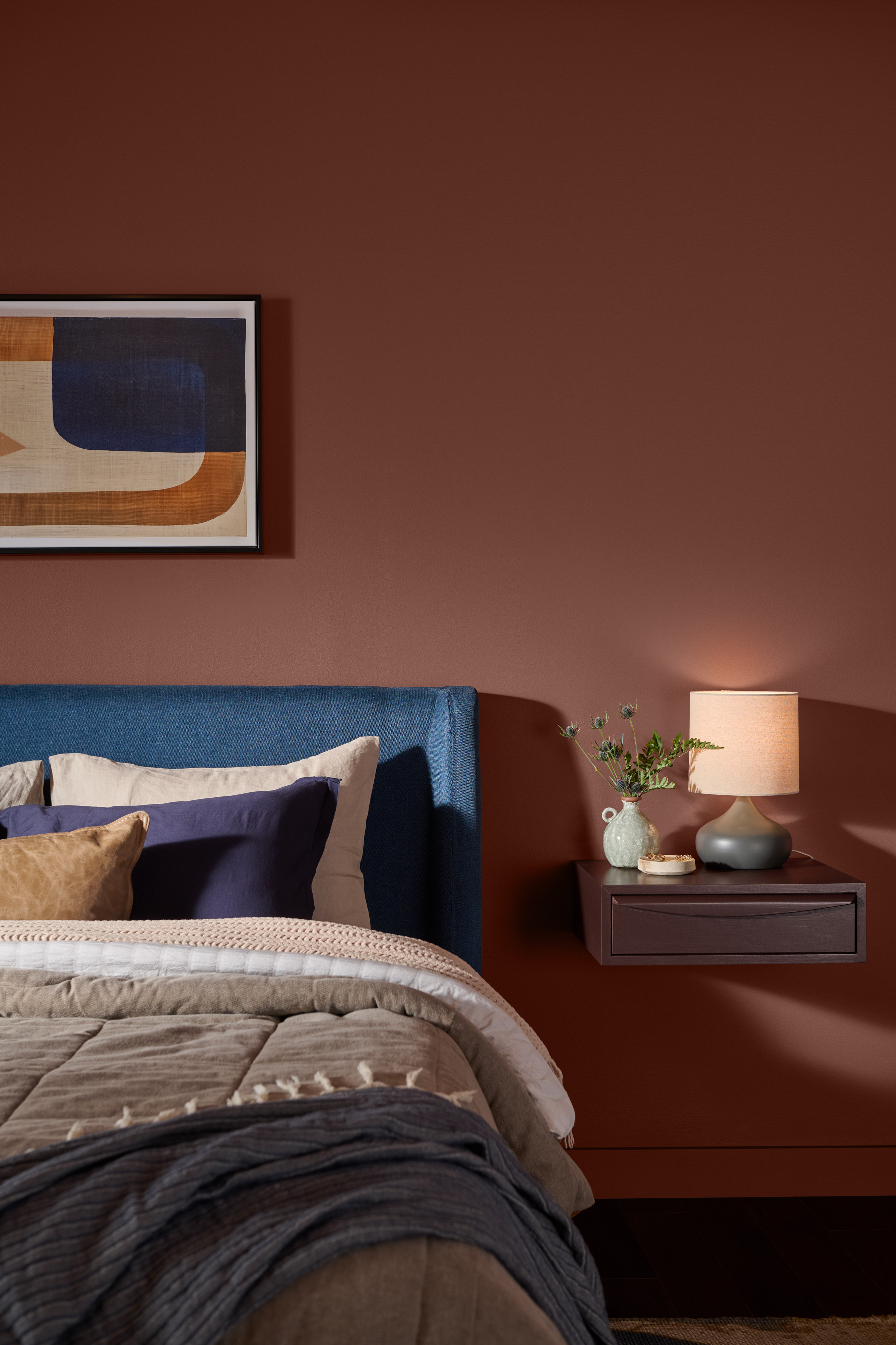 Bedroom with walls painted Tuscan Terra T27-02, a warm clay-toned colour paired with blue, grey, and neutral bedding, natural wood, and soft lighting.