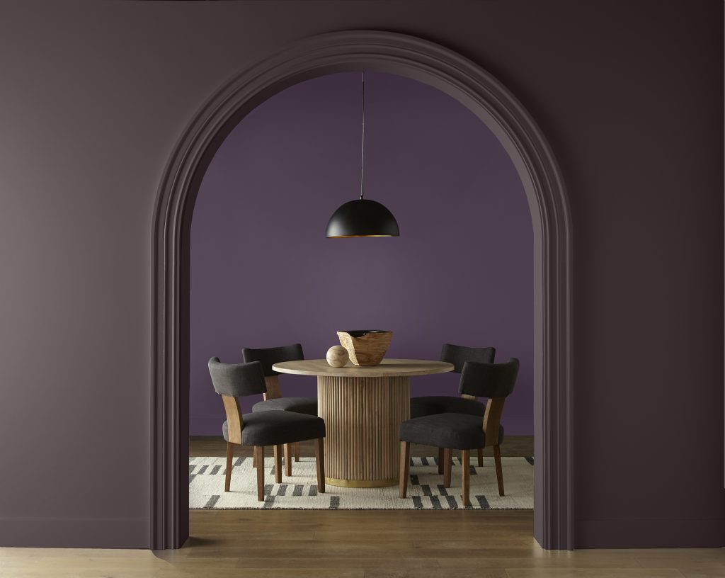 Dining room with Deep Merlot M100-7 walls revealed through an arched opening framed by Sarsaparilla HDC-AC-26, with a round wood table, dark chairs and black pendant light.