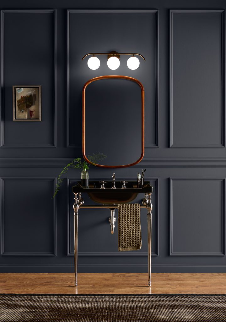 Bathroom with paneled walls painted Nightfall T27-04, paired with a dark console sink, warm metallic mirror and fixtures, wood flooring and black accents.