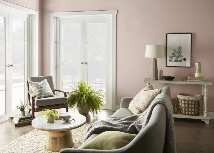 A bright living room painted in BEHR® Smokey Pink with crisp ULTRA PURE WHITE® trim. Two large windows fill the space with natural light, while neutral furnishings, warm wood tones, and fresh greenery create a soft, airy feel.
