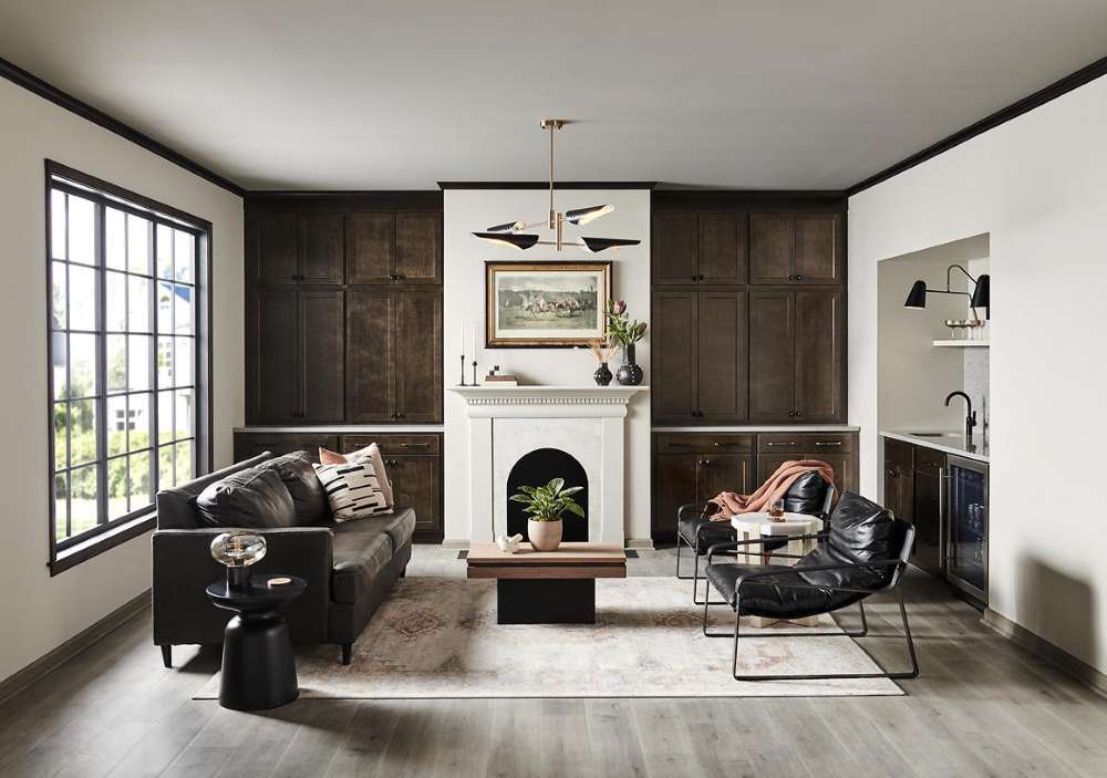 A sophisticated contemporary living room with walls painted Tranquil Gray and trim painted BLACK. Dark wood built-ins, black leather seating, a white fireplace, black-framed windows, and warm wood accents create a tailored, high-contrast look. Soft natural light and a muted neutral palette keep the space feeling balanced, polished, and inviting.