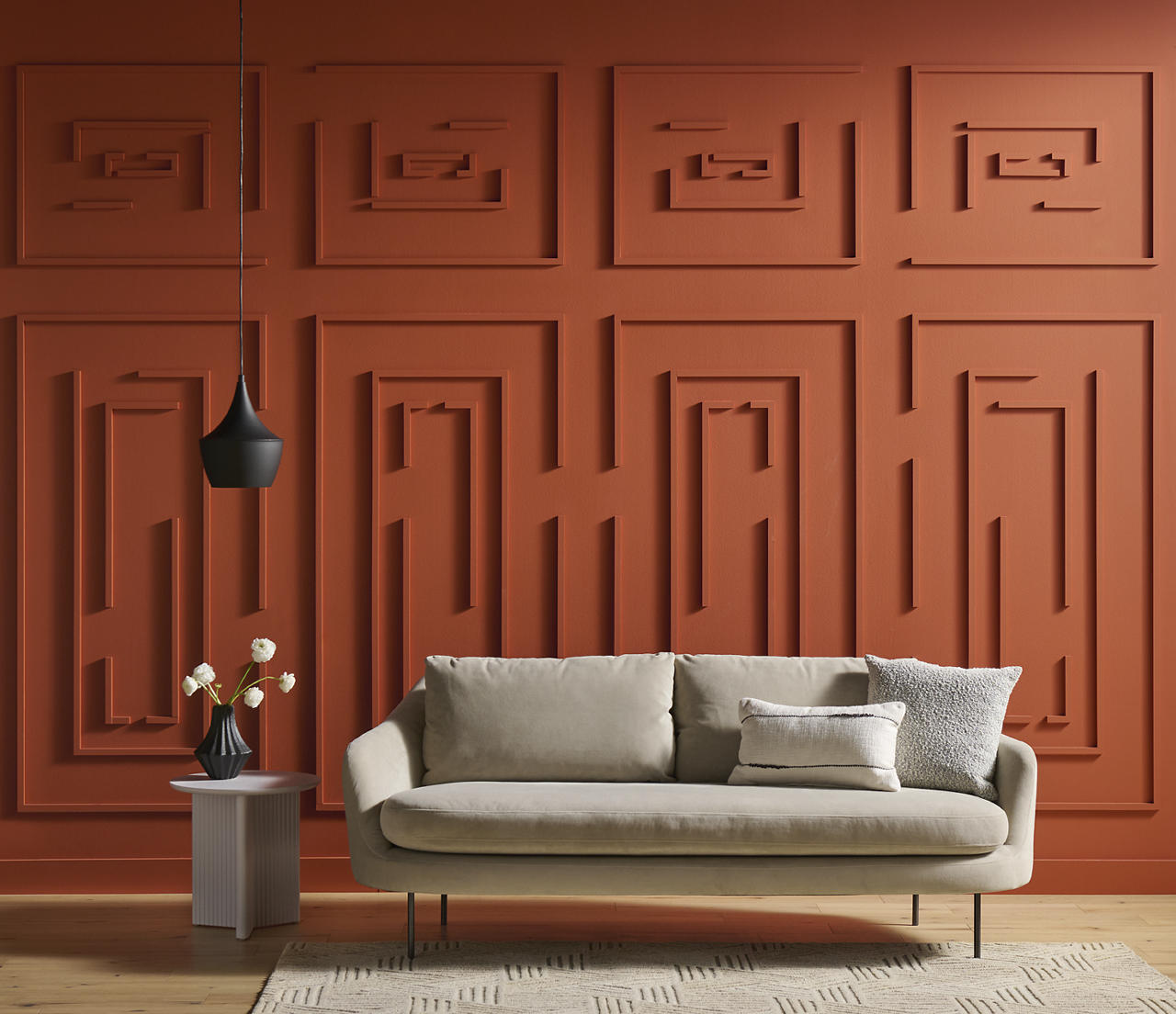 A living room featuring BEHR® Colorful Leaves on the walls with decorative paneling arranged in a geometric maze pattern, paired with warm neutral furnishings, natural wood tones, and layered textures for a cozy, distinctive look.