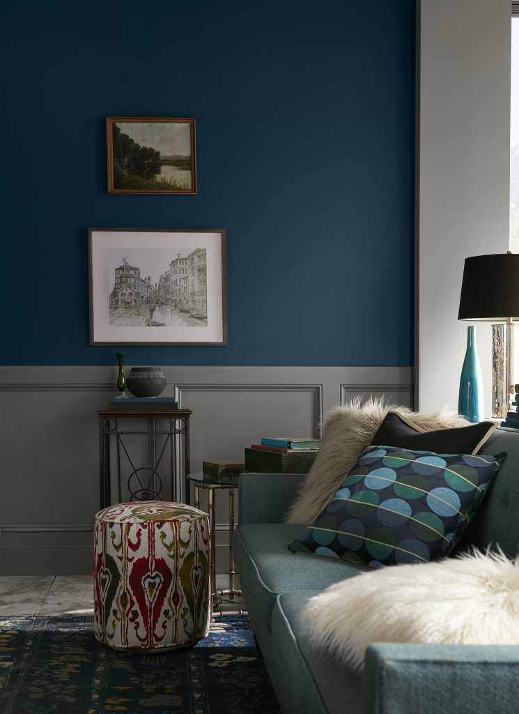 Living room with upper walls painted Nocturne Blue HDC-CL-28 above grey paneled wainscoting, paired with teal seating, patterned textiles and warm wood accents.